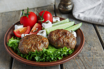 fried cutlets in plate with vegetables on wooden table