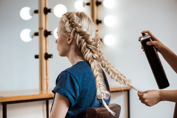 Female hairdresser making hairstyle to blonde girl in beauty salon.