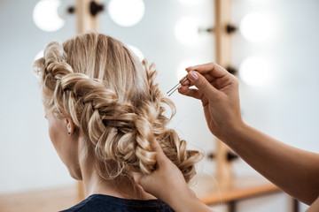 Female hairdresser making hairstyle to blonde girl in beauty salon. - obrazy, fototapety, plakaty