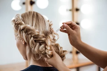 Fototapeten Female hairdresser making hairstyle to blonde girl in beauty salon. © Cookie Studio