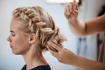 Rolgordijnen Female hairdresser making hairstyle to blonde girl in beauty salon. © Cookie Studio