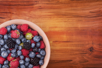 Brown ceramic plate with berries on the left bottom corner of the wooden table with clipping path. Top view.