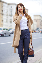 Fototapeta premium Portrait of happy young brunette woman in beige coat talking on