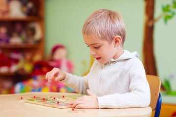 cute boy, kid with special needs solving a puzzle in rehabilitation center