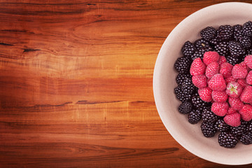 Ceramic plate with heart shaped berries on the right of the wooden table with clipping path. Top view.