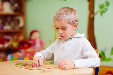cute boy, kid with special needs solving a puzzle in rehabilitation center