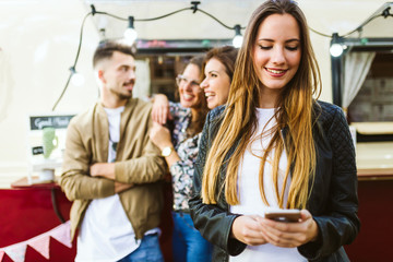 Beautiful young woman with her friends using mobile phone.