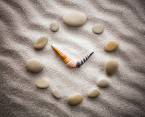 Stylized dial clock pebble and shells arrows on the sand for concentration and relaxation for harmony and balance in pure simplicity - macro lens shot