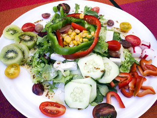 Colorful plate of fresh mixed salad of goat cheese chunks, sliced cucumber, tomato, pepper, radish, lettuce, kiwis, grapes