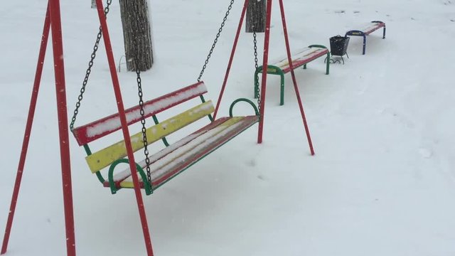 Empty swing in winter time with snow.