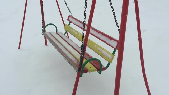 Empty swing in winter time with snow.