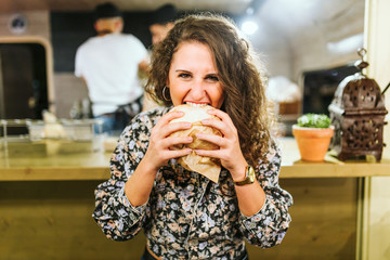 Beautiful young woman eating hamburguer in the food truck.