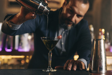 Barman is making cocktail at night club.