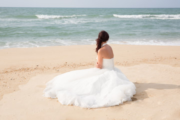 Fototapeta na wymiar Bride sitting along sea coast in the wedding dress