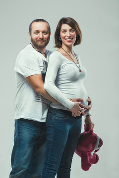 Young couple standing in embrace and looking at the camera, pregnant woman