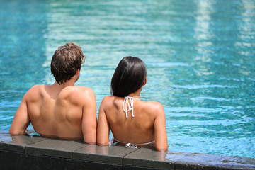 Honeymoon couple relaxing on the edge of an infinity swimming pool in luxury resort spa retreat....