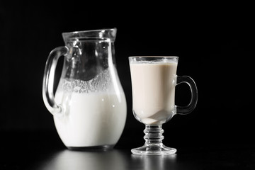 Milk is from jug bottle into the glass on black background.