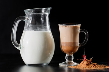 Milk is from jug bottle into the glass on black background.