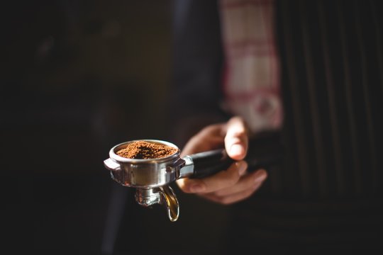 Mid section of waiter holding portafilter filled with ground cof