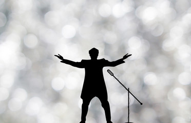 Silhouettes of showman singer with microphone on blured silver shiny background