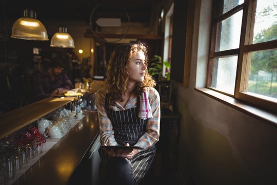 Thoughtful waitress looking through window in cafe