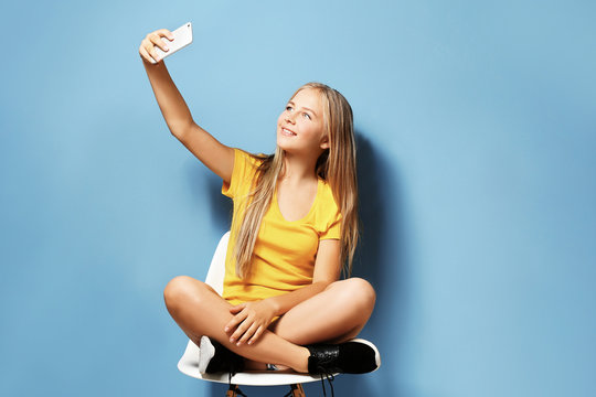 Cute teenager girl taking selfie on blue background