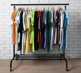 Colorful t-shirts on hangers against brick wall