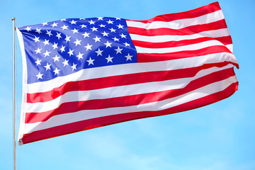 Ruffled American flag on blue sky background.