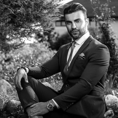 Black-white outdoor portrait of elegant handsome man in classical suit.