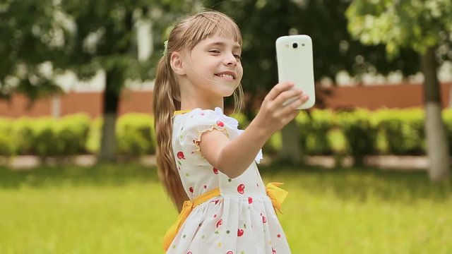 Little girl in a white dress makes selfi on the meadow.