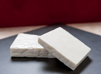 Buffalo paneer Indian cheese on black slate cutting chopping board counter in two large pieces stacked diagonally on top of each other with copy space above and dark red background