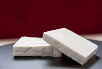 Buffalo paneer Indian cheese on black slate cutting chopping board counter in two large pieces stacked diagonally on top of each other with copy space above and dark red background