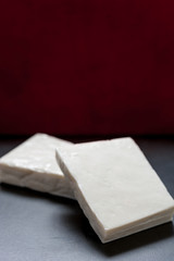 Buffalo paneer Indian cheese on black slate cutting chopping board counter in two large pieces stacked diagonally on top of each other with copy space above and dark red background