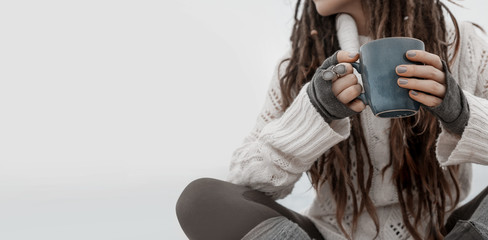 close up of young woman in sweater sitting on beach, holding cup