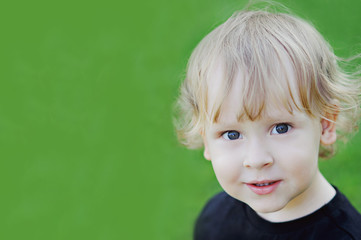Portrait of a blond curly-headed boy on green background, close-up, copy space.