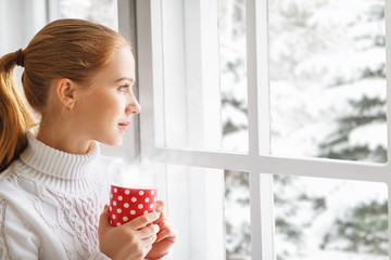 happy young woman with cup of hot tea in winter window Christmas