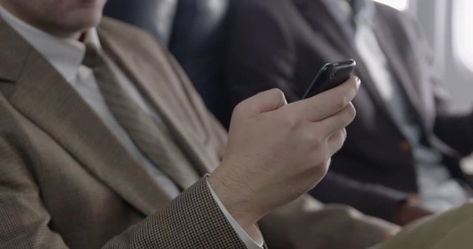 Business men using mobile phones in first class section of commercial airliner.  Detail view of Caucasian man's hand with camera dolly movement.