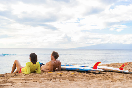 Couple surfers relaxing after surfing on hawaiian beach. Two people lying down on sand beach at sunset next to surfboards after a surf class on Kaanapali beach in Maui, Hawaii island, USA.