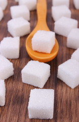 Wooden spoon with cubes of sugar on wooden background