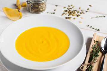Pumpkin cream-soup in plate close-up. Top view on bowl with bright orange soup puree, spoon and squash seeds.