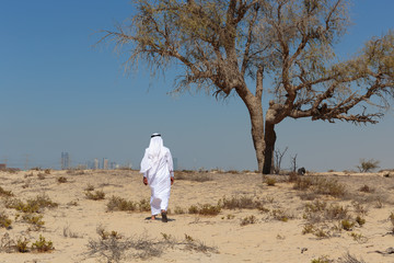 Arab man in national dress stands in the desert and looks at the