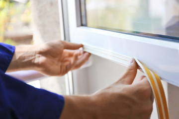 Construction worker putting sealing foam tape on window in house