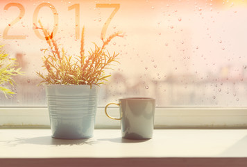 Coffee cup on table with rain drop and 2017 text on window backg
