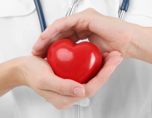 Female doctor with stethoscope holding heart, closeup