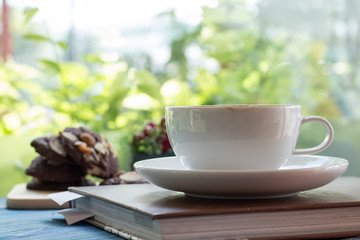 A cup of coffee with chocolate cookie on blue wooden table and green garden background.