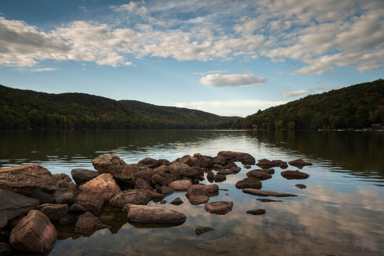 a mountain pond with sky reflection and rocks in the foreground in autumn in New England
