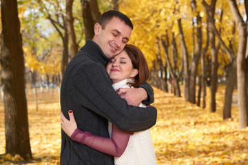 romantic people, happy adult couple embrace in autumn city park, trees with yellow leaves, bright sun and happy emotions, tenderness and feelings