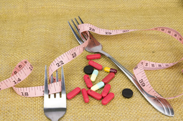 Risk diet and healthy concept - Steel spoon a fork, pills and measuring tape with shallow depth of field (dof)