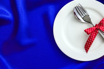  White empty plate with fork and spoon and red ribbon on luxury