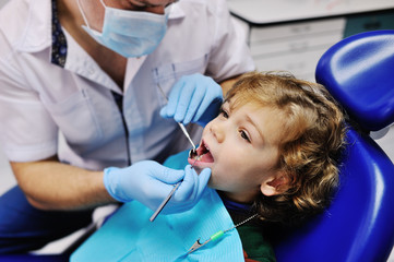 Male dentist examines the teeth of the patient cheerful child with curly red hair. Moloi boy smiling in dentist's chair. child mouth wide open in the dentist's chair